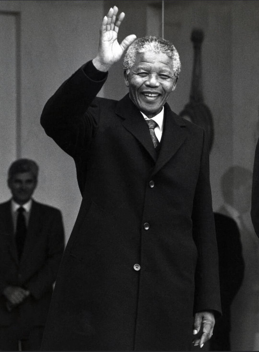 Photographie en noir et blanc de Nelson Mandela souriant et levant la main en signe de salutation